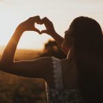 femme formant un cœur avec ses mains au coucher du soleil symbole de santé du cœur et circulation sanguine