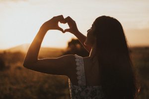 femme formant un cœur avec ses mains au coucher du soleil symbole de santé du cœur et circulation sanguine