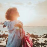 femme face au soleil en bord de mer symbolisant énergie, bien-être et vitalité du corps