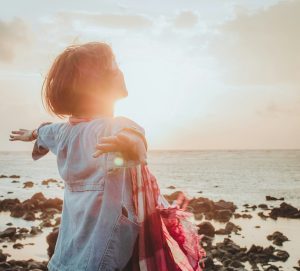 femme face au soleil en bord de mer symbolisant énergie, bien-être et vitalité du corps